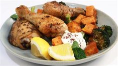 a white plate topped with chicken, broccoli and sweet potatoes next to lemon wedges