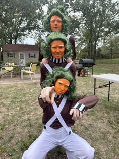 three people wearing green wigs and holding scissors in front of their faces while standing on the grass