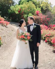 a bride and groom standing on a dirt road in front of colorful flowers at their wedding