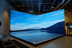 a large projection screen in the middle of a room with mountains and water on it