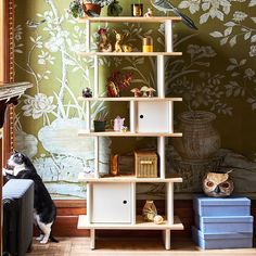 a cat sitting on the floor next to a book shelf with birds and flowers painted on it