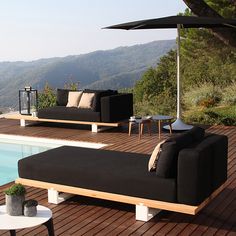 a black couch sitting on top of a wooden deck next to a swimming pool with mountains in the background