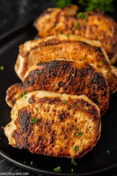 grilled pork chops on a black plate with parsley