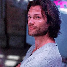 a man with long hair standing in front of a tv screen and looking off to the side