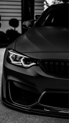 the front end of a black car parked in a parking lot next to a garage