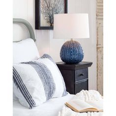 a blue vase sitting on top of a nightstand next to a book and lamp in a bedroom