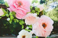 three pink and white flowers are in a vase on the table outside with greenery