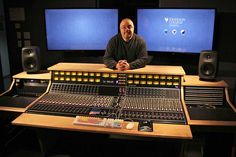 a man is sitting in front of two monitors and sound mixing equipment on a desk