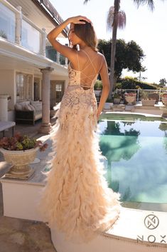 a woman standing next to a swimming pool wearing a dress with feathers on the skirt