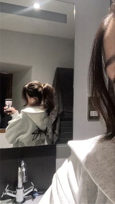 a woman taking a selfie in front of a bathroom mirror while brushing her hair