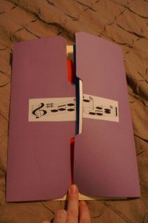 a hand holding an open purple book with musical notes on the pages and a red pen sticking out of it