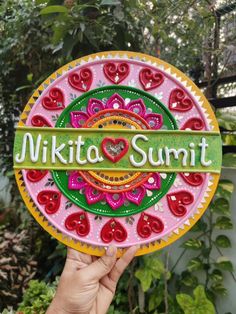 a hand holding up a sign that says mikta summit in front of some plants