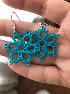 a hand holding a pair of earrings in it's left hand, with blue beads on them