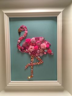 a pink flamingo made out of buttons and flowers in a white frame on a blue wall