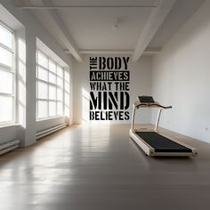 an empty room with a treadmill in the foreground and a quote on the wall above it