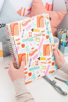 a person is holding a notebook in front of some crafting supplies on a table