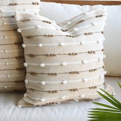 two white pillows sitting on top of a couch next to a plant in a vase