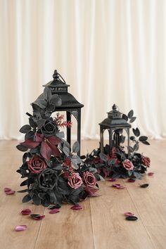 two small black lanterns with flowers on the floor next to each other and petals scattered around them