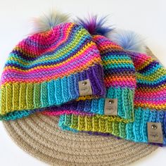 three knitted hats with fur pom - poms on top of each other