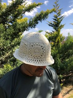 a man wearing a white crochet hat while standing in front of some trees