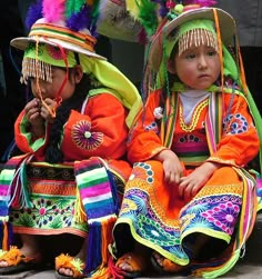 two young children dressed in colorful costumes and headdress sitting next to each other