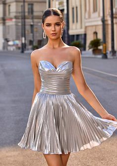 a woman is walking down the street wearing a silver dress with pleated skirt and high heels