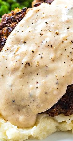 a white plate topped with mashed potatoes and meat covered in gravy next to broccoli