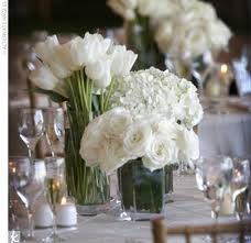 there are many white flowers in vases on the table with wine glasses and candles