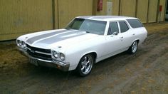 an old white station wagon is parked in front of a building on a dirt road