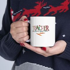 a woman holding a white coffee mug with the word teacher written on it in red