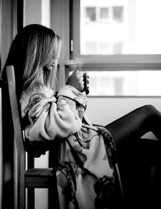 a woman sitting in a chair with her legs crossed and looking out the window,