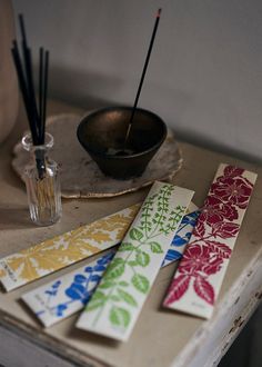 four different colored papers sitting on top of a table next to a bowl and cup