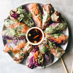 a white plate topped with rolls covered in veggies and dipping sauce next to chopsticks