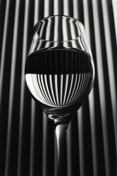 a wine glass sitting on top of a table next to a black and white striped wall