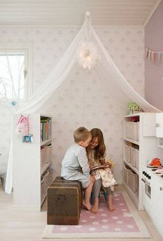 two children are sitting in a room with pink and white wallpaper on the walls