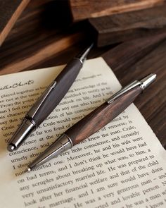 two fountain pens sitting on top of an open book next to a pen and paper