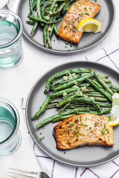 two plates with salmon, asparagus and green beans on them next to glasses of water