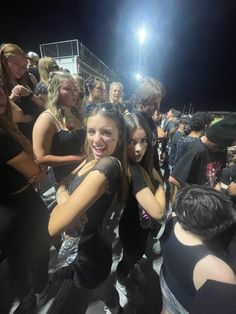 two young women standing next to each other in front of a group of people at night