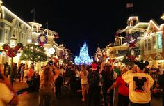 people are walking down the street in front of christmas lights and buildings at disneyland world