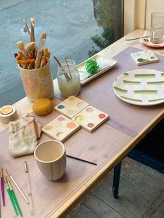 a wooden table topped with lots of crafting supplies next to a glass and window