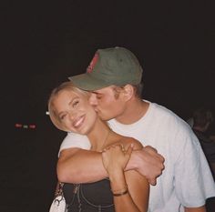 a man and woman hugging each other in front of the camera at night time,