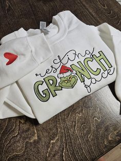 This ADORABLE crewneck sweatshirt is the perfect apparel for the Christmas season! It is super soft and fleece lined. You also get the option to choose 1 of many designs to go on the right sleeve.  Don't see a color sweatshirt you like? Easy! Just message me with a color you had in mind, and I will see if I can get it for you! **please note: Due to the big variety of color options, I order the sweatshirts after you have purchased- so the vendor I use sometimes runs out of specific colors in spec Grinch Sweater Cricut, Christmas Grinch Shirt Ideas, Christmas Crew Neck Sweatshirt With Embroidered Logo, Christmas Embroidery Sweatshirts, Grinch Sweaters, Christmas Sweatshirts Vinyl, Sweatshirt Design Ideas, Grinch Sweatshirt, Resting Grinch Face