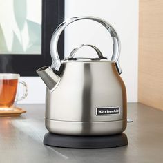 a tea kettle sitting on top of a wooden table next to a cup of tea