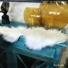 a blue table topped with two vases and a white fur covered chair leg rest