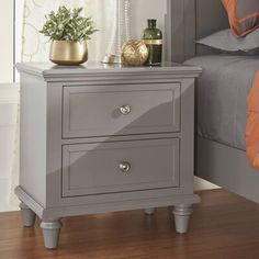 a nightstand with two drawers and a lamp on top of it next to a bed