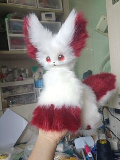 a hand holding a stuffed animal with red eyes and white fur on it's body