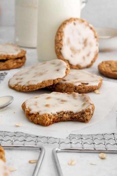 some cookies with icing on a table next to a glass of milk and two spoons