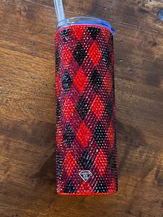 a red, black and white plaid flask on a wooden table with a toothbrush in it