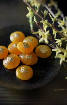 small oranges on a black plate next to some flowers