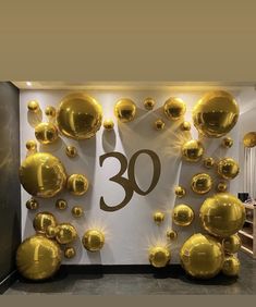 the number 30 is surrounded by golden balloons in front of a white wall with gold numbers on it